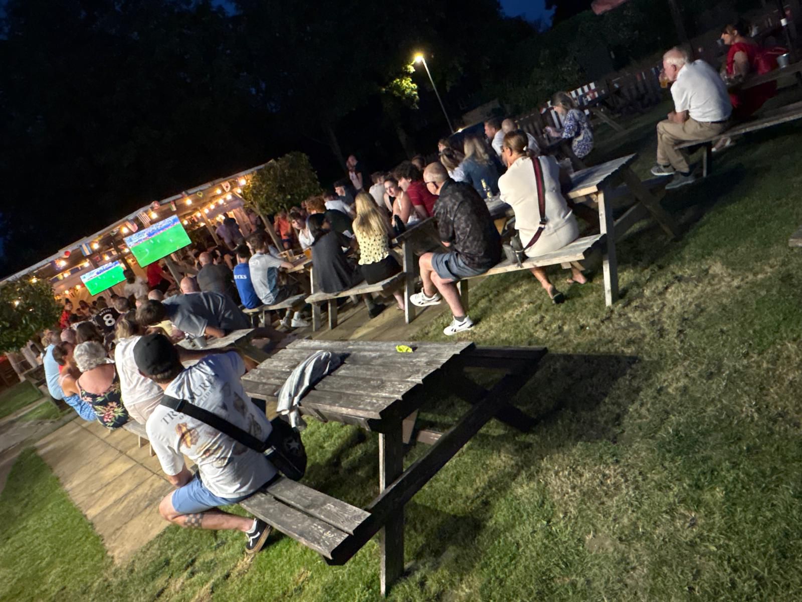 People watching football on a large outdoor screen in the garden after dark